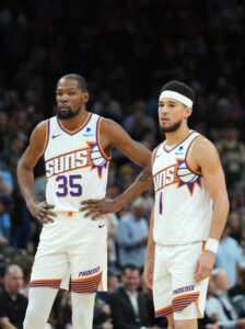 Mar 20, 2024; Phoenix, Arizona, USA; Phoenix Suns forward Kevin Durant (35) and Phoenix Suns guard Devin Booker (1) look on against the Philadelphia 76ers during the first half at Footprint Center. Mandatory Credit: Joe Camporeale-USA TODAY Sports